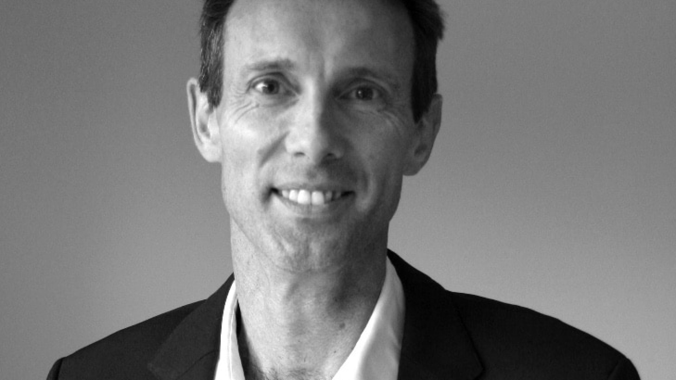 Jonathan Grant, Secretary General of the International Aluminium Institute, smiles slightly at the camera in a suit jacket and white shirt, set against a plain background.